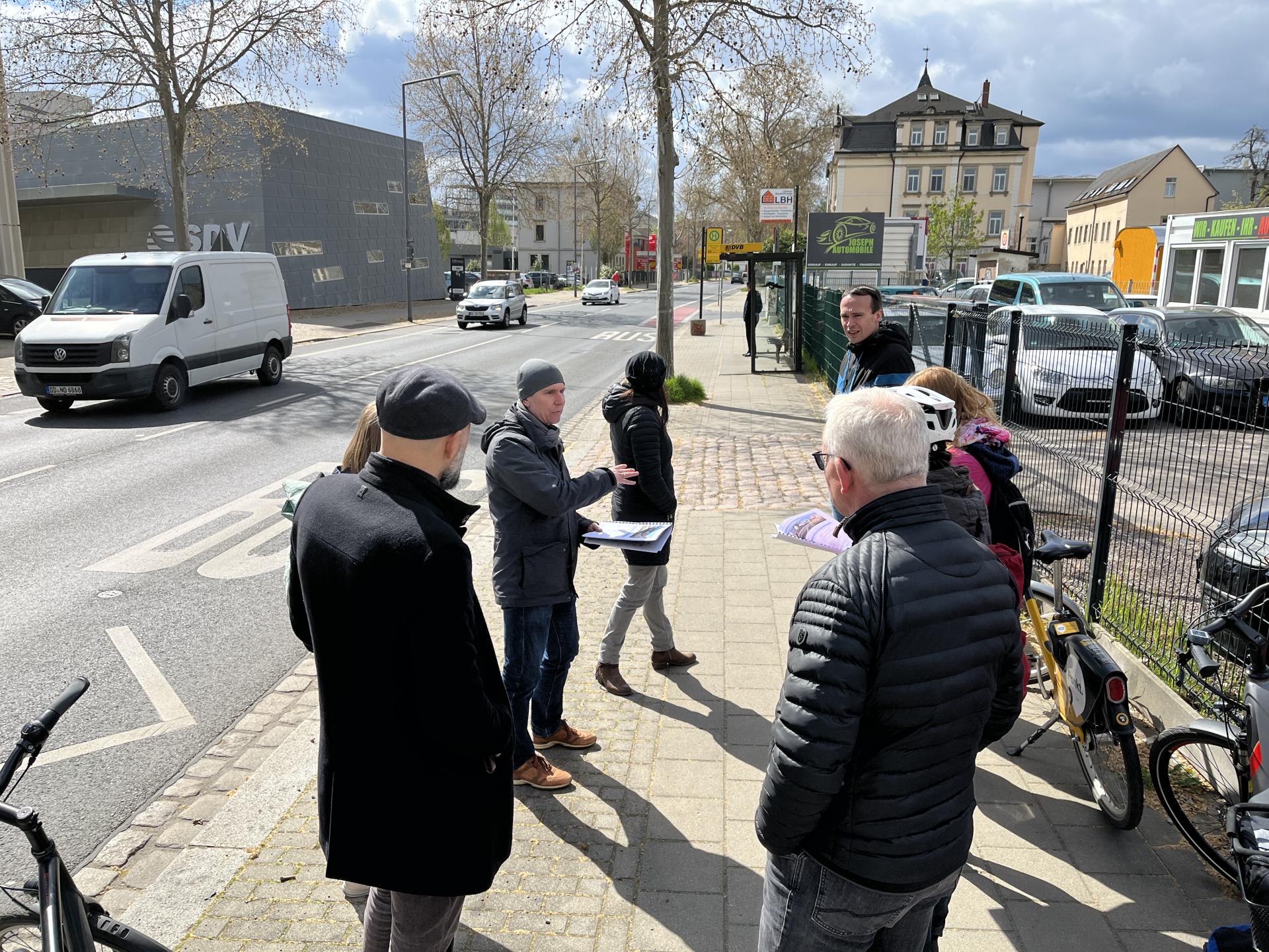 Eine Gruppe von Personen steht auf dem Gehweg und diskutiert.