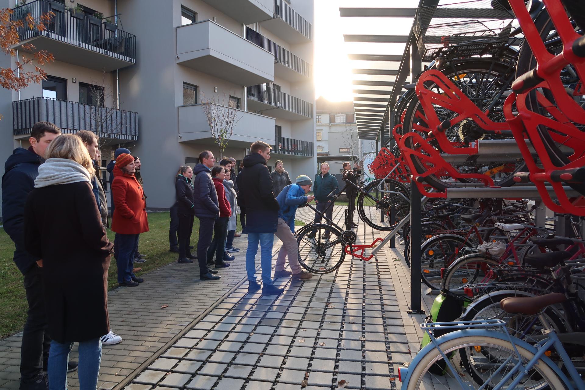 Personen sehen zu wie eine Person ein Fahrrad in eine Schiene einer Radabstellanlage schiebt.