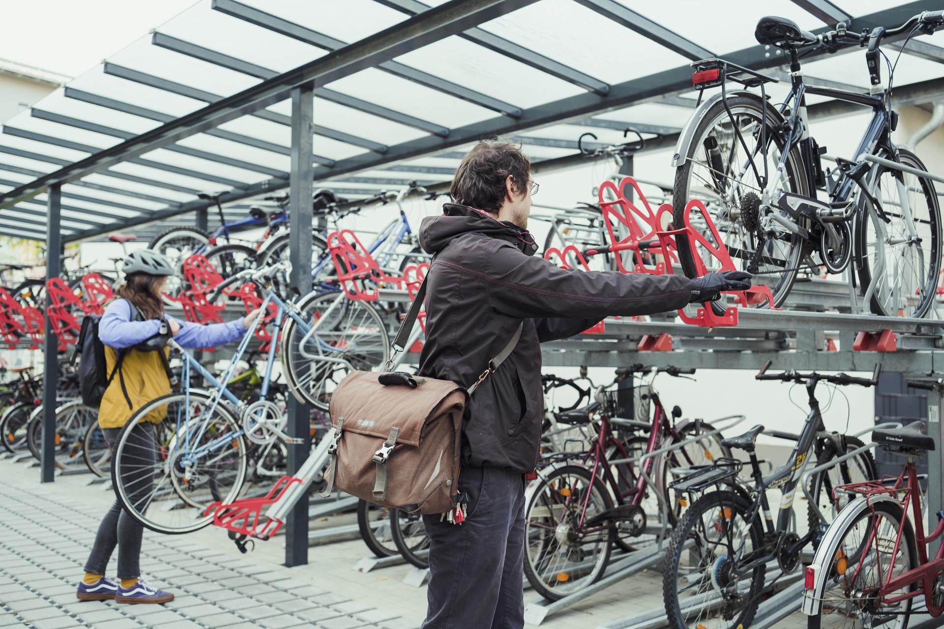 Zwei Personen schieben ihre Fahrräder in Schienen einer Radabstellanlage.