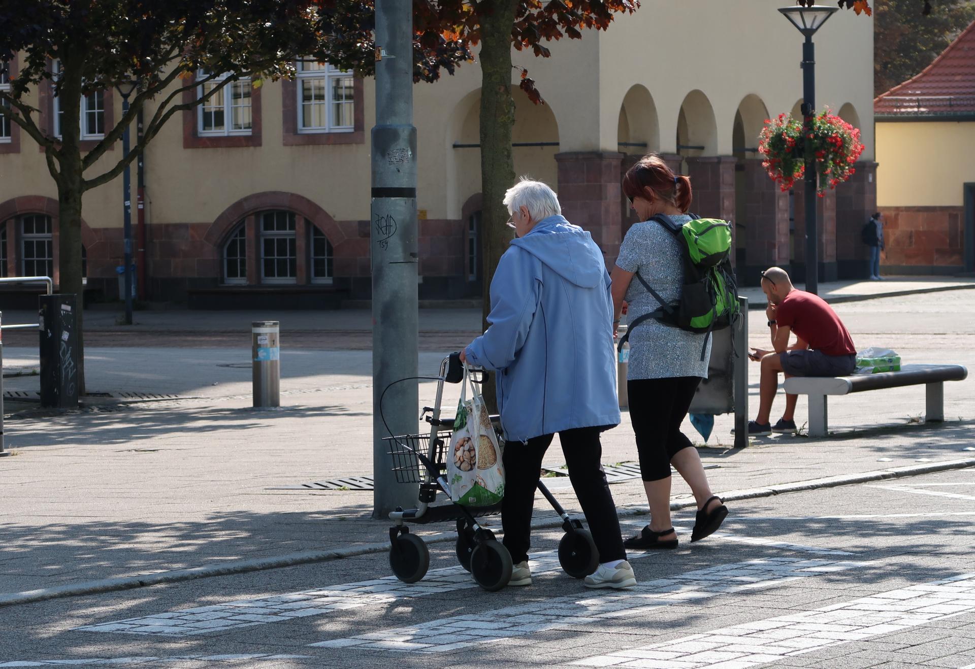 Zwei Frauen gehen vor dem Rathaus über einen Zebrastreifen, eine geht mit einem Rollator.