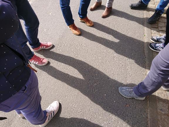 Beine und Füße einer auf der Straße stehenden Gruppe von Personen.